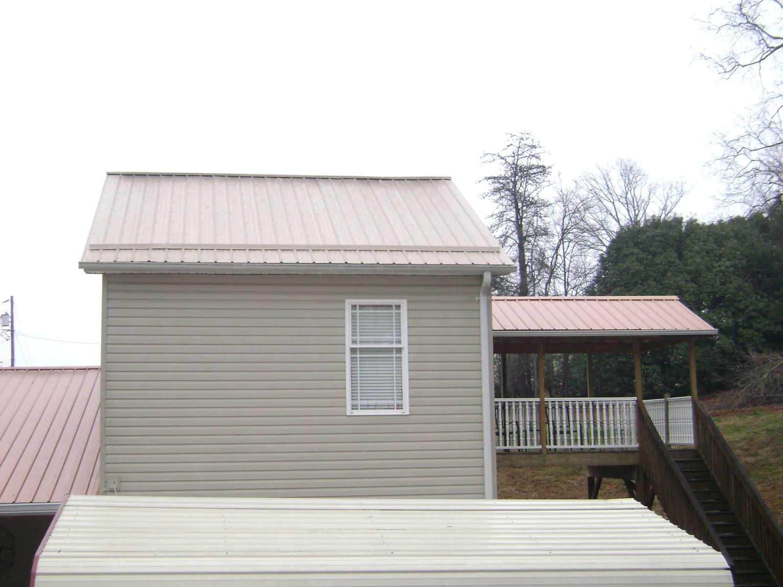Tan metal roofs on a two story addition and attached porch, from a Roof Replacement job in Bedford